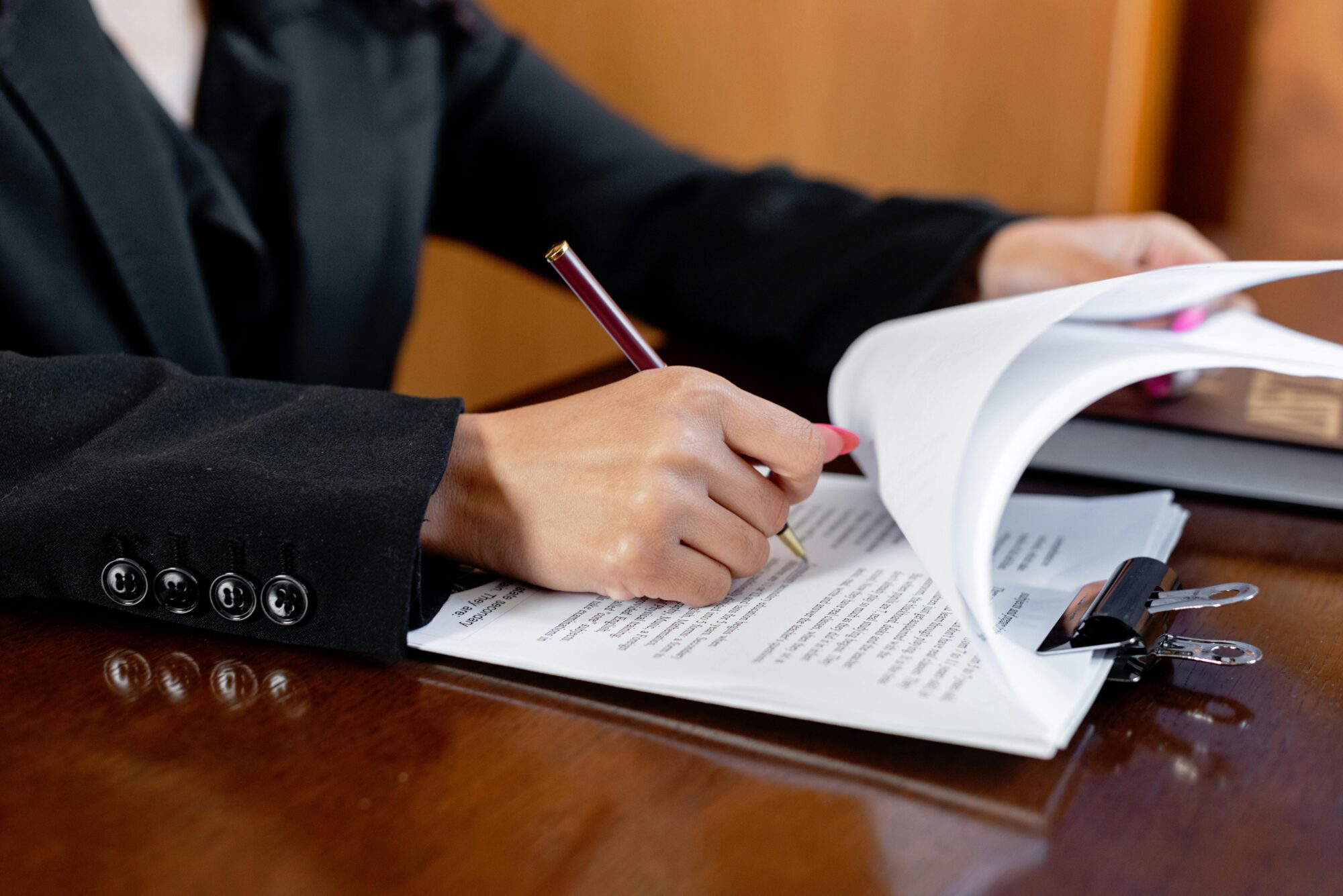 Close-up of a woman signing legal documents with a pen in an office setting.